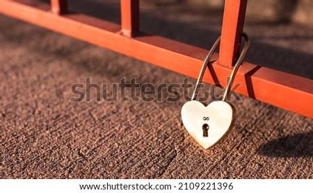 Golden shiny heart shape padlock with infinity icon above keyhole hold at the bottom of red bridge with bright sunlight. Symbol for loyalty, forever mutuality and strengthening love. Valentine concept