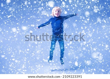 The boy spread his arms out to the sides and bounces in place. Child catches snowflakes with his hands
