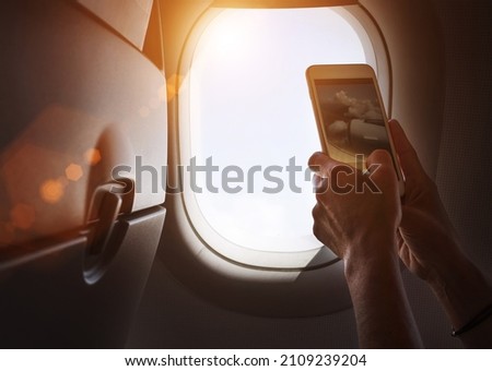 Female using her smartphone for photographing clouds and aircraft engine through the porthole. Active traveling and flying by planes aviation transport concept image.