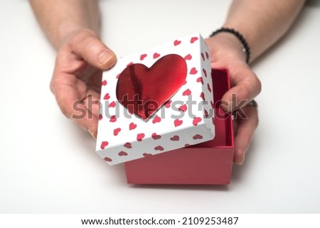 Closeup of hands of woman opening  a red and white carton box with printed hearts on white background