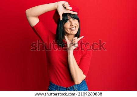 Young hispanic woman wearing french look with beret smiling making frame with hands and fingers with happy face. creativity and photography concept. 