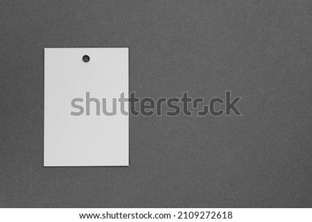 Brand label tag of white color made of cardboard for clothes with little hole in top part placed on left on dark gray background. Tag mock up. Copy space.