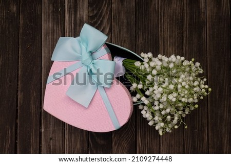 A small bouquet of lilies of the valley lies in a heart-shaped gift box.