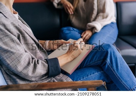 Close-up of a psychologist's hands writing down notes about a patient in a notebook. The psychologist makes a social survey of the reference group. A professional is talking to a client. Royalty-Free Stock Photo #2109278051