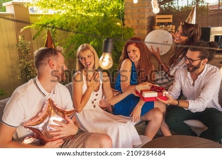 Group of cheerful young friends having fun at birthday party, birthday girl receiving presents
