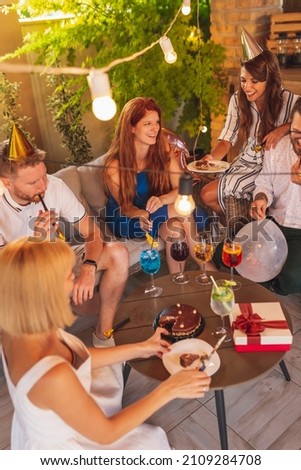 Group of cheerful young friends having fun at a birthday party, hostess cutting and sharing birthday cake