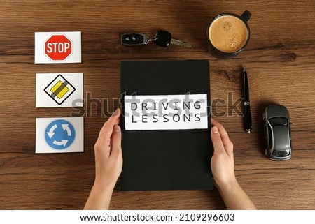 Woman with workbook for driving lessons and cup of coffee at wooden table, top view. Passing license exam