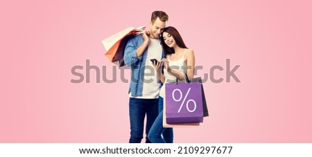 Holiday sales actions, rebates, discounts offers concept image - happy couple with shopping bags, looking at mobile smart phone, isolated over pink color background. % sign. Valentines Day holiday.