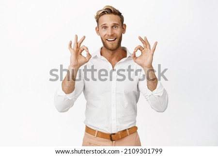 Portrait of smiling blond man in shirt, showing okay signs, give approval, satisfied with smth, standing against white background