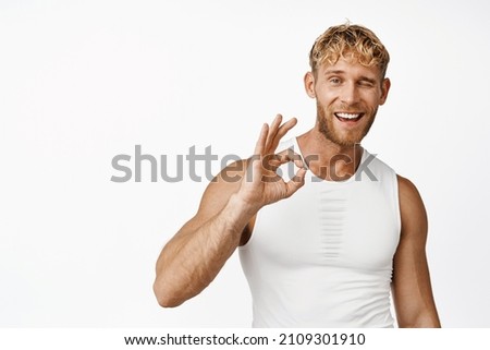 Image of fitness athlete showing okay sign and winking, sportsman smiling and showing praise, white background
