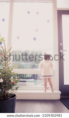 Curious girl on window ledge below Christmas ornaments