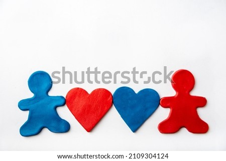 Blue and red plasticine people hold red and blue plasticine heart shapes in their hands on a white background