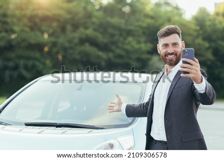 Successful and happy man brags about buying a new car, having fun talking to friends uses a video call in the phone app Royalty-Free Stock Photo #2109306578
