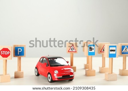 Many different miniature road signs and car on white wooden table, space for text. Driving school