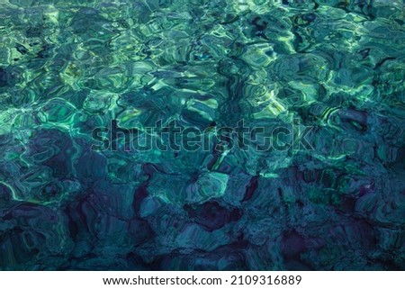 Sea rocky bottom under transparent blue water. Clear turquise lake surface rippled with sun ray reflection.