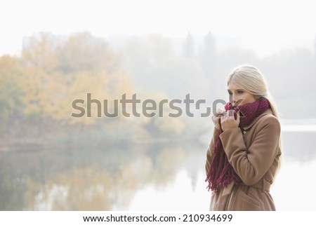 Thoughtful young woman wearing muffler at lakeside in park