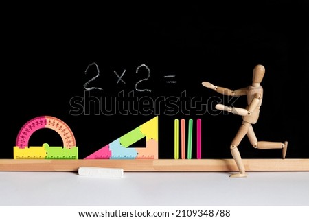 wooden mannequin as a teacher or pupil against blackboard with equation and bright colorful school accessories