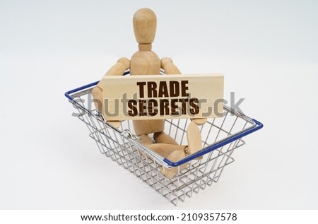 Business and finance concept. A wooden man sits in a shopping basket, holding a sign in his hands - TRADE SECRETS