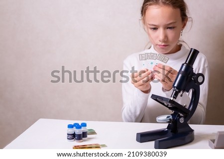 A schoolgirl with a microscope examines chemicals in test tubes, conducts experiments. The concept of coronavirus research in the laboratory. High quality photo