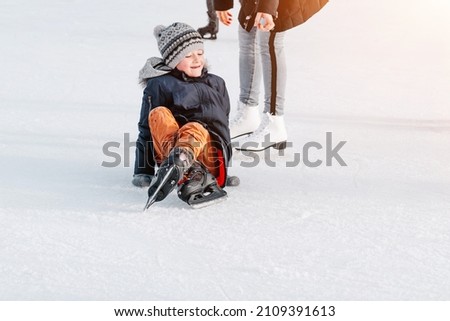 Mom with baby boy ,learn train, ride winter city rink, ice skating.The child gets up,fell on skates, kneels, play fun rest on weekend first steps child skates.The child fell on the rink while skating.