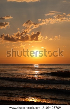 
Summer sunset on the sea, the sun sets over the horizon, waves rise, white clouds in the sky.
