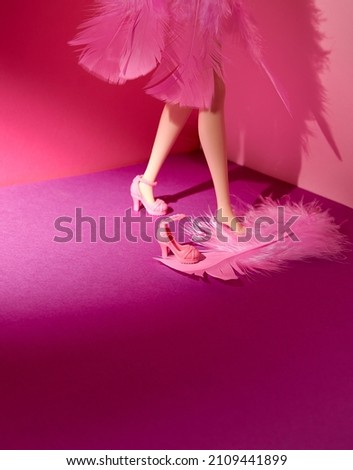 A woman doll dressed in pink feathers and pink high-heeled shoes. Bright pink and purple background. Text space. Lifestyle, fashion, glamor, concept. Minimal style. Royalty-Free Stock Photo #2109441899