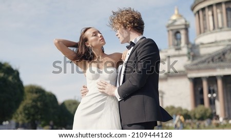 Beautiful newlyweds on background of old architecture. Action. Elegant couple of newlyweds posing on background of cathedral on sunny day. Newlyweds on windy sunny day in summer Royalty-Free Stock Photo #2109444128