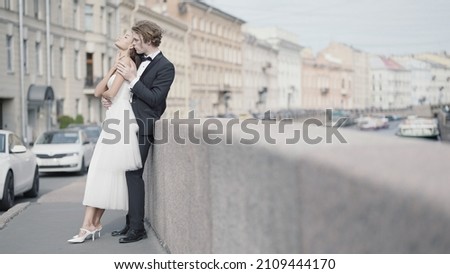 Beautiful couple of newlyweds embracing on background of city. Action. Photo shoot for newlyweds in urban environment. Beautiful newlyweds embrace in city with old architecture Royalty-Free Stock Photo #2109444170