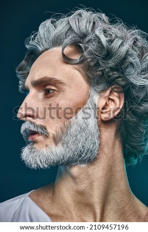 Art image of God. Close up shot of a divine man with curly grey hair and beard posing in profile on a blue background. Roman and Greek mythology, Christianity and religion. Royalty-Free Stock Photo #2109457196