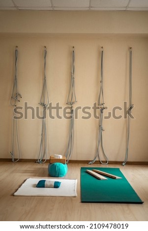 Empty fly yoga Iyengar class with inventory for physical training. Yogi props rope on wall, wooden plank, bolster weighting agent with sand, brick and strap. Professional supply for therapy workout