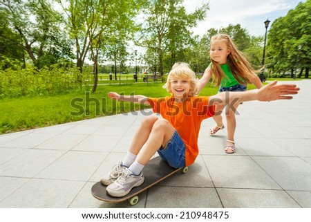Small girl pushing happy boy on skateboard