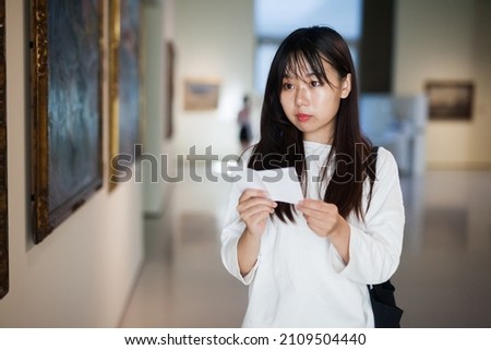 Chinese woman standing with guide-book in art museum near the painting in baguette