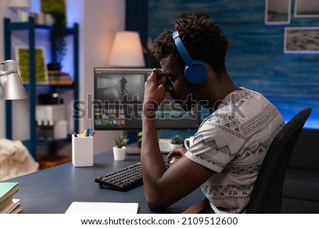 Professional artist editor sitting at desk table in creativity studio working remote from home at film montage using post production software. Tired videomaker editing movie footage creating content