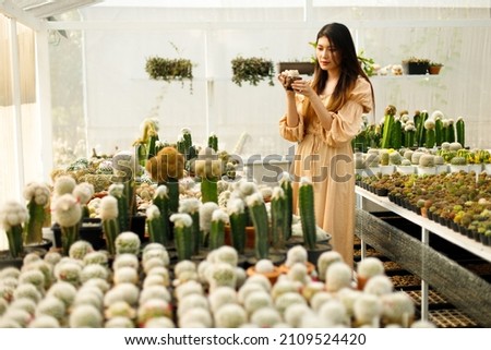 Cactus plant in woman hands looks relax style concept. 20s Asian female black straight hair feel happy smile in Greenhouse farm variety Cactus seed nursery, horizontal copy space