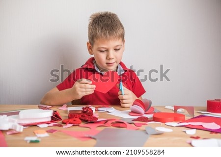DIY holiday card with red paper heart, symbol of love. Kid boy makes Mother's Day, Valentine's Day, greeting card. Hobby, children art concept, gift with your own hands, DIY Ideas for children