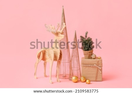 Wooden reindeer with small Christmas tree, present and decor on pink background