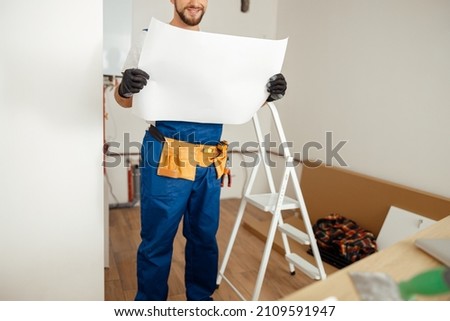 Cropped shot of construction worker looking at blueprint while standing in new apartment