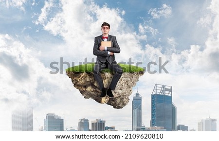 Young student with a book sits on a flying island. The cityscape in the background