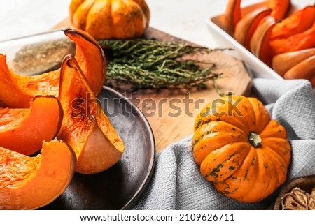 Plate with baked pumpkin pieces and fresh vegetable on light background, closeup