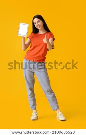 Beautiful teenage girl with tablet computer showing thumb-up on yellow background
