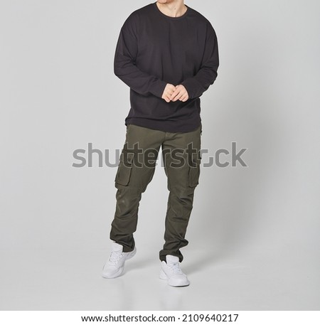 Cropped shot of man in black blank long sleeved and green cargo pants. Standing on gray background. Mockup for print or design template. Basic clothing line no logo Royalty-Free Stock Photo #2109640217