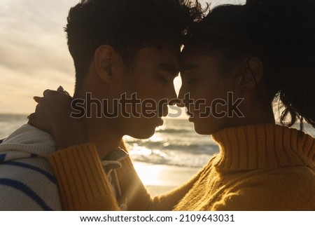 Side view of multiracial couple romancing while hugging each other at beach during sunset. lifestyle, love and weekend. Royalty-Free Stock Photo #2109643031