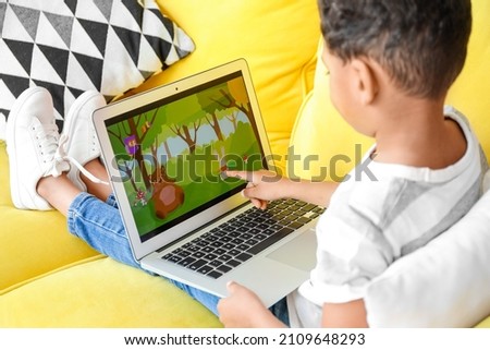 Little African-American boy pointing at laptop while watching cartoons on sofa at home Royalty-Free Stock Photo #2109648293