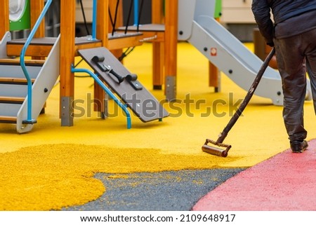Laying a rubber coating of crumbs on a children's playground. Roller leveling rubber mulch. Royalty-Free Stock Photo #2109648917