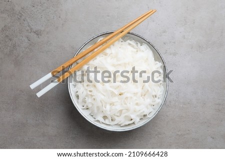 Bowl with cooked rice noodles and chopsticks on light grey table, top view