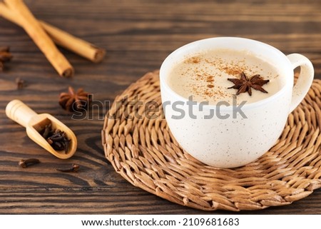 Masala tea with milk, cloves and anise in a mug on a wooden table.