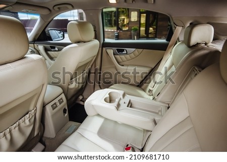 Luxury car interior made of white leather. Leather folding armrest armrest with cup holders in rear seats inside a vehicle. Clean leather interior: white rear seats, headrests and belts. Royalty-Free Stock Photo #2109681710