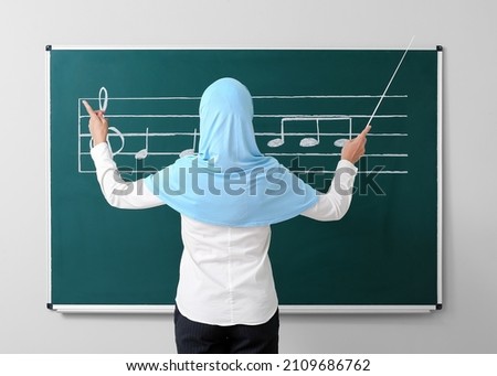 Muslim music teacher near blackboard in classroom