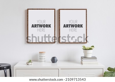 Minimalistic home decor of interior with two brown wooden mock up photo frames on the white shelf with books, beautiful plant in stylish pot and home accessories. White wall.
