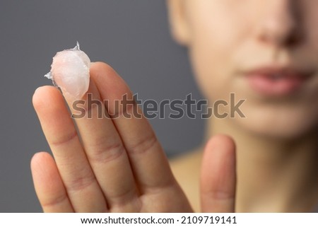 A young woman is applying petroleum jelly to her face. Concept of slugging. Royalty-Free Stock Photo #2109719141